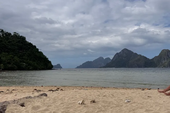 An empty beach with limestone islands in the distance under a cloudy sky.
