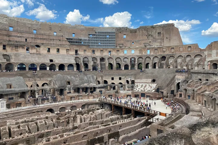 The inside of the Colosseum, with the arena floor open to view and visitors on a walkway.