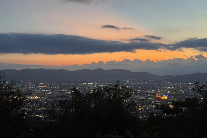 The city of Kyoto below, with an orange band of sky above distant mountains at dusk.