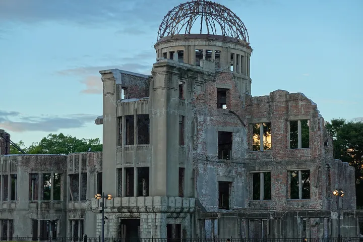 The ruined dome of the Hiroshima Peace Memorial in late sun, with trees behind.