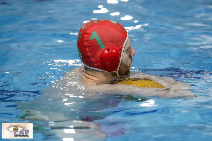 A water polo player in a red cap treading water during a match.