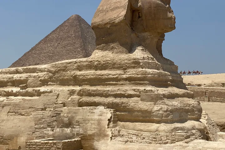 The Great Sphinx of Giza, with a pyramid behind it under a clear sky.