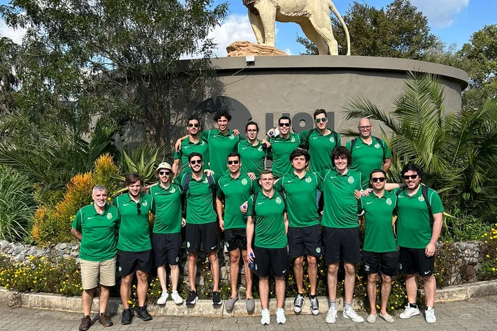 A squad in green kit posing in front of a large stone lion.
