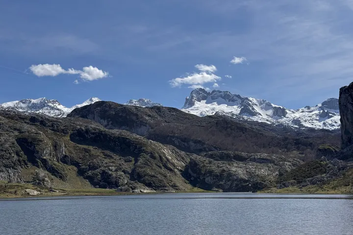 A mountain lake with snow-capped peaks behind it and a few clouds in a blue sky.
