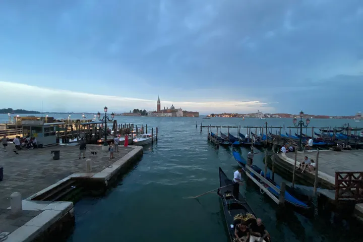 Gondolas moored along a quay at dusk, with the island of San Giorgio Maggiore across the water.