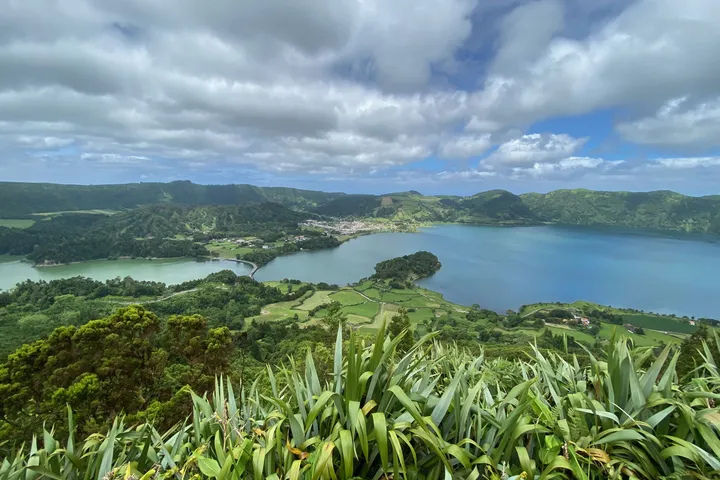 Two crater lakes seen from a viewpoint, with tall grasses in the foreground and clouds above.