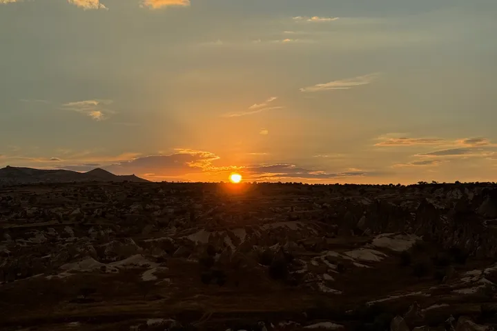 The sun low over a dark, rocky valley, with gold light through the clouds above.