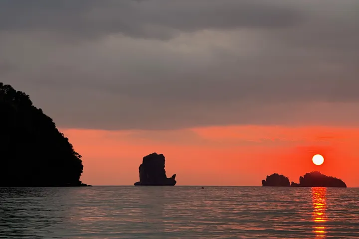 A red sun setting behind limestone islets, under heavy dark clouds.