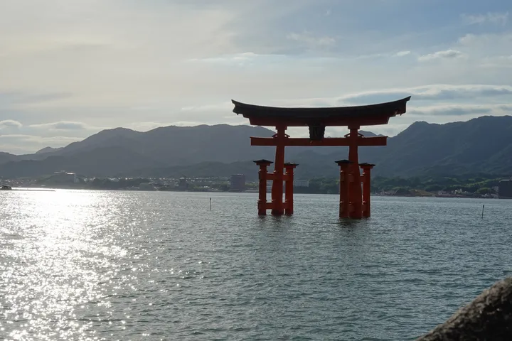 The red torii of Itsukushima shrine standing in the sea, with hills behind under a hazy sky.