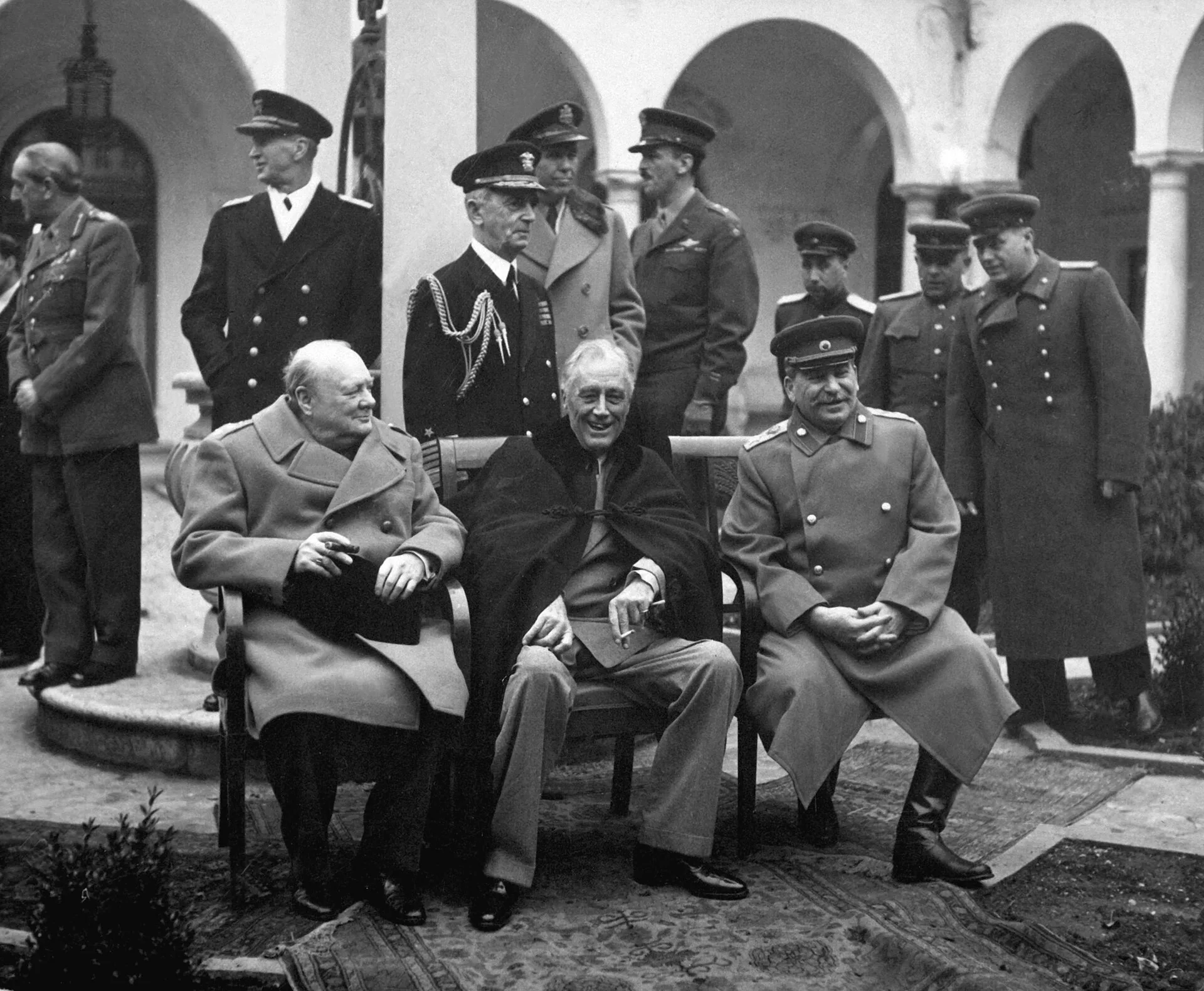 Churchill, Roosevelt and Stalin seated together at the Yalta Conference, with their military advisers standing behind them